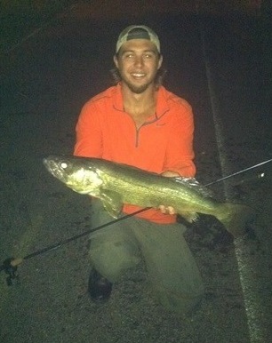 night time picture of a person with a fishing pole holding a large fish